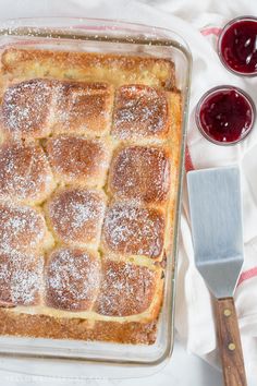 a baking dish with powdered sugar on top and two cups of jelly in the background