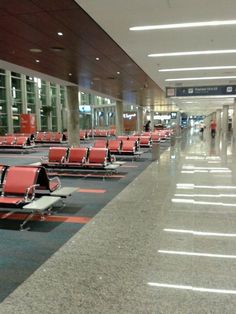 rows of red chairs sitting in an airport terminal waiting for passengers to arrive or depart