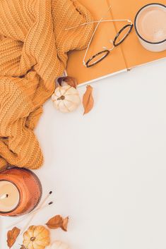 an overhead view of pumpkins, candles and glasses on a white surface with a yellow blanket