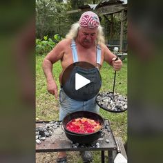 a man cooking food on top of a grill in the grass with an iron skillet