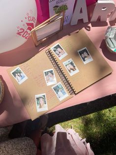 an open notebook with photos on it sitting on top of a pink table next to other items