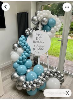 a happy 18th birthday balloon arch with blue, silver and white balloons in front of a window