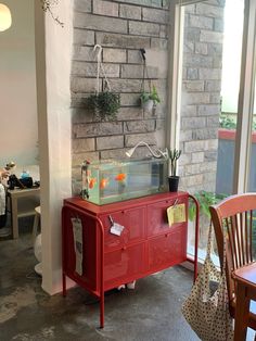 a red cabinet with plants on it in front of a brick wall and window sill