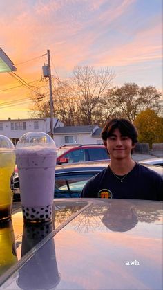 a man sitting at a table with two drinks in front of him and the sun setting behind him