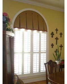 a dining room with yellow walls and white trim on the windowsills is decorated with crosses