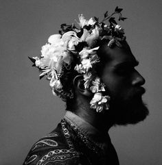 a black and white photo of a man with flowers in his hair, looking off to the side