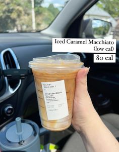 a person holding up a cup of iced caramel macchato in their car