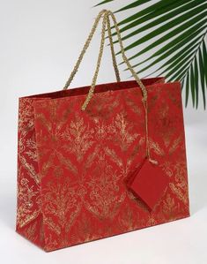 a red shopping bag hanging from a gold chain on a white background with palm leaves