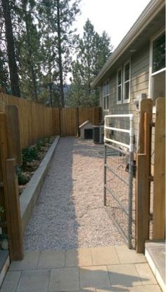 a fenced in area with gravel and plants on the side walk leading to a house