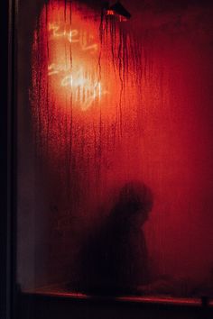 a person standing in front of a window with red light coming from it's side