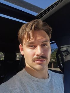 a man with a mustache is sitting in the back seat of a car and looking at the camera