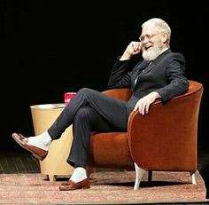 an older man sitting in a chair talking on the phone