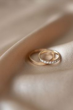 two gold wedding rings sitting on top of a white cloth