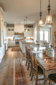 a kitchen and dining room area with wooden table, chairs, rugs and pendant lights