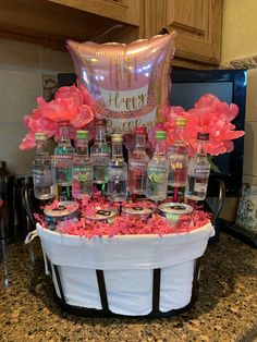 a table with bottles and balloons on it in the shape of a basket filled with pink flowers