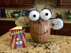 a book sitting on top of a kitchen counter next to a fake pumpkin shaped like a bug