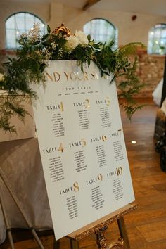 a table plan with flowers and greenery on it sitting on a stand in the middle of a room