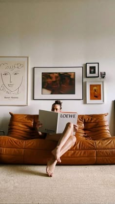 a woman sitting on top of a brown couch holding a book in front of her face