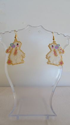 a pair of earrings is displayed on a clear display stand with a white wall in the background