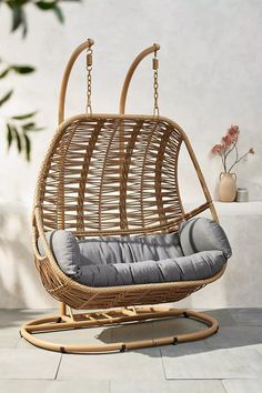 a rattan swing chair with grey cushions on a tiled floor next to a potted plant