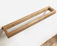 a wooden shelf with two handles hanging on it's side against a white wall