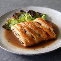 a white plate topped with pastry next to a green leafy salad on top of a table