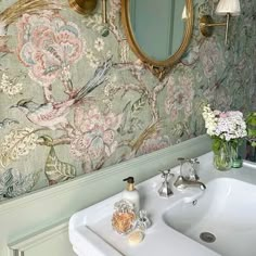 a bathroom sink sitting under a mirror next to a wall mounted faucet with flowers on it