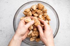 two hands reaching for small pieces of food in a glass bowl on a gray surface