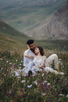 a man and woman sitting on top of a lush green hillside