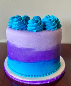 a cake with blue frosting and purple icing on a wooden table next to a white wall