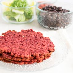 two red patties are sitting on a glass plate next to some black beans and lettuce