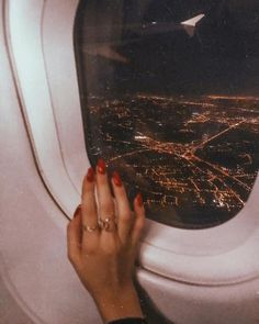 a woman's hand is on the window of an airplane at night with city lights in the background