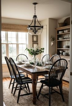 the dining room table is set for four with black chairs and white dishes on it