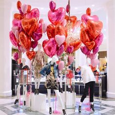 people are standing in front of large balloons on display at a storefront with pink and red heart shaped balloons hanging from the ceiling