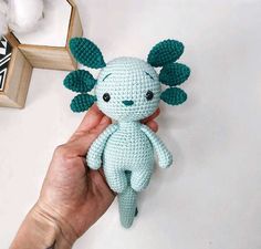 a hand holding a small crocheted stuffed animal in front of a mirror with cotton balls