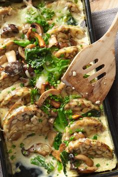 a casserole dish with mushrooms, spinach and other vegetables in it next to a wooden spatula