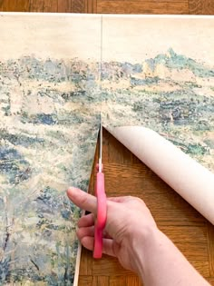 a person is cutting up some fabric with scissors on a table next to a painting