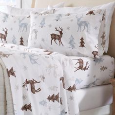 a bed covered in white and brown sheets with reindeers on them, sitting next to a window