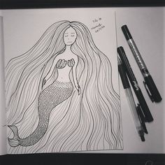 a drawing of a mermaid sitting on top of a table next to some markers and pens