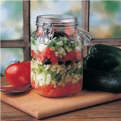 a wooden cutting board topped with a glass jar filled with salad and veggies