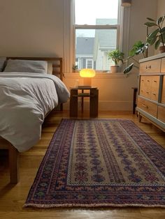 a bedroom with a bed, dresser and rug on the wooden floor next to a window