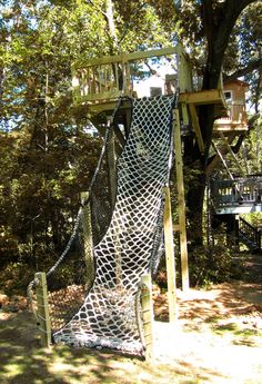 a tree house with a climbing net on the top and stairs up to the bottom