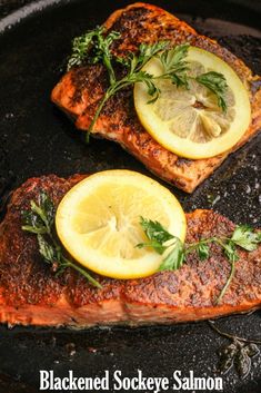 two salmons with lemon slices and herbs on them in a cast iron skillet