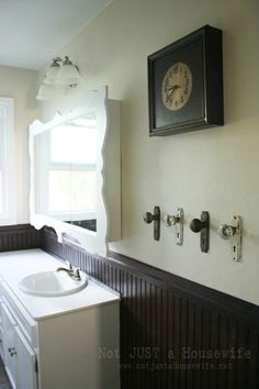 a white sink sitting under a window next to a clock mounted on the side of a wall