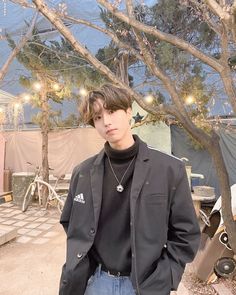 a young man standing in front of a tree with lights strung from it's branches