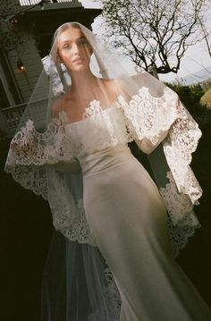 a woman wearing a wedding dress and veil in front of a house with an overhang