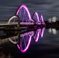 a bridge that is lit up with purple lights and reflecting in the water at night