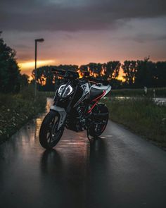 a motorcycle parked on the side of a wet road at night with trees in the background