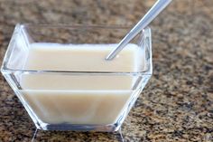 a glass bowl filled with milk on top of a counter next to a metal spoon