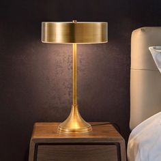 a gold lamp on a night stand next to a bed